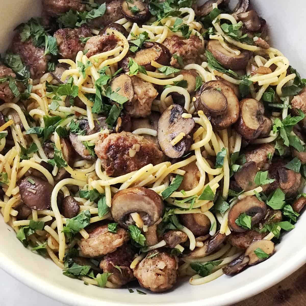 Spaghetti with mushrooms and sausage in a white bowl