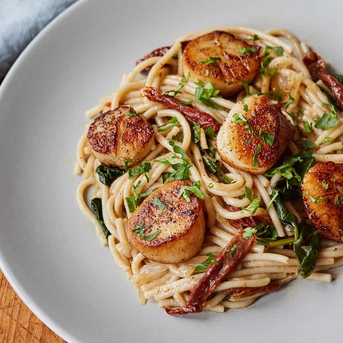Tuscan Spaghetti with Scallops served on a light gray plate on wooden surface