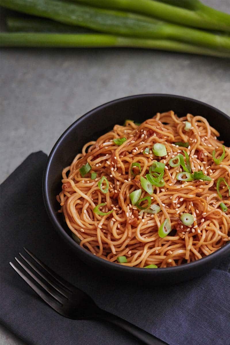 Spicy Sesame Garlic Ramen Noodles served in black bowl next to black napkin on metal surface