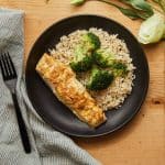 Roasted Dijon Halibut served with brown rice and broccoli on a black plate