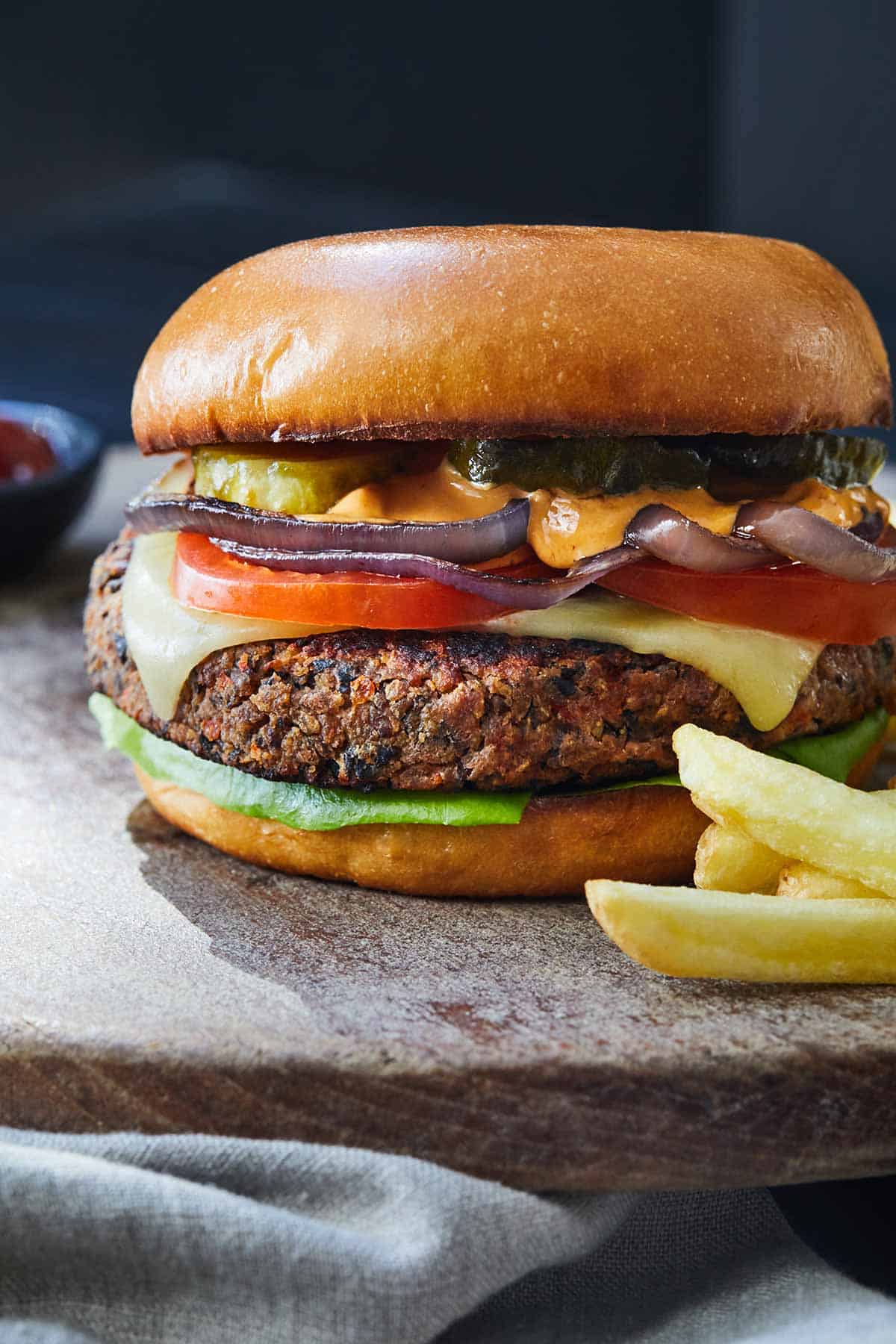A black bean burger on a wooden serving board with fries.