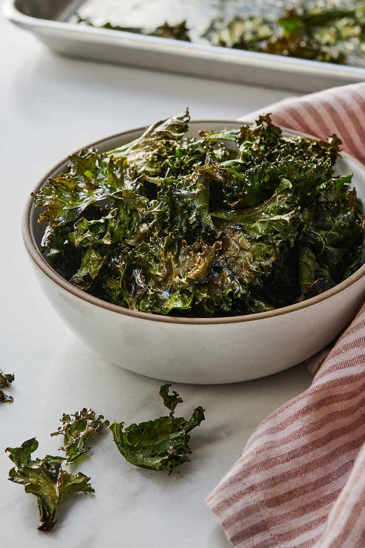A bowl of crispy kale chips beside a pink and white linen.