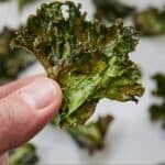 Pinterest graphic of a hand holding up a piece of kale chips.