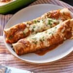 Pinterest graphic of a plate of two enchiladas on a pink and white linen.
