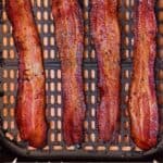 Pinterest graphic of an air fryer basket with four strips of bacon.