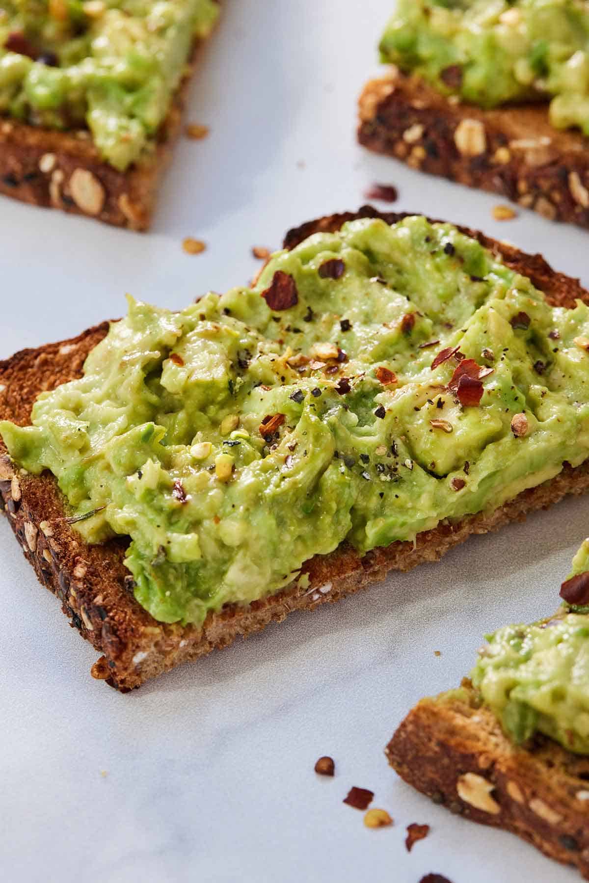 Close up of a half slice of avocado toast with red chili flakes on top.