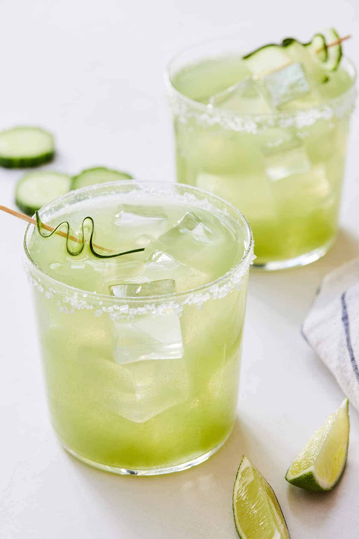 Two glasses of cucumber margarita with salted rims and cucumber garnish.