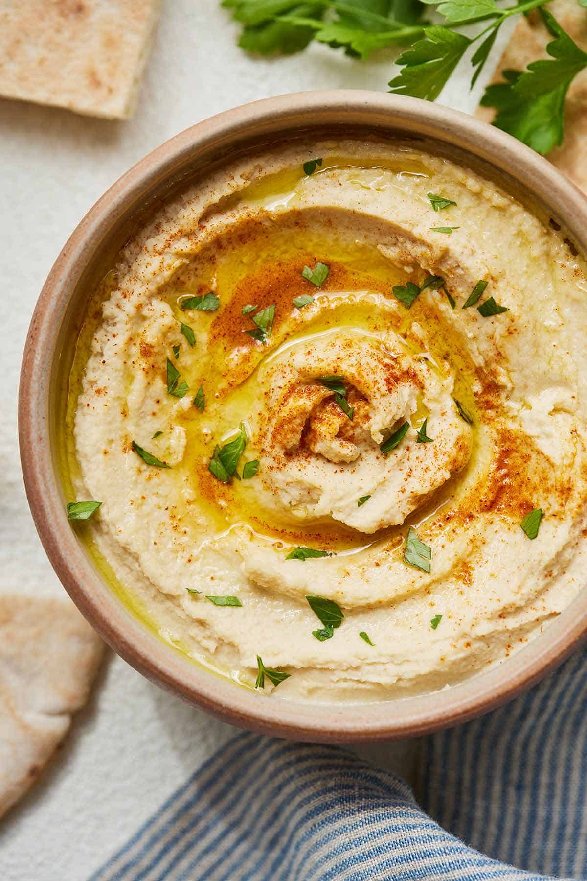Overhead view of a bowl of hummus with pita bread around it.