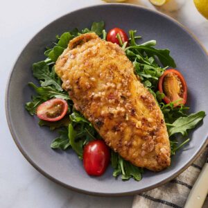 Chicken paillard in a plate over greens and tomatoes.