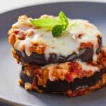 Close up of a serving of eggplant parmesan with melted cheese and basil on top.