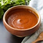 Red enchilada sauce in a bowl beside cilantro and a linen.