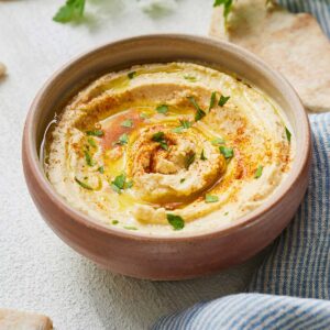 A bowl of hummus beside a linen and pita bread.