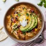 Overhead view of a bowl of Instant Pot chicken tortilla soup topped with shredded cheese, sour cream, and sliced avocado.