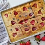 Close up of a sheet pan pancake beside a linen, strawberries, and chocolate chips.