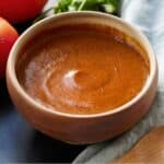 Pinterest graphic of a bowl of enchilada sauce with a linen and tomatoes beside it.