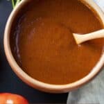 Pinterest graphic of an overhead view of a bowl of enchilada sauce with a spoon inside.