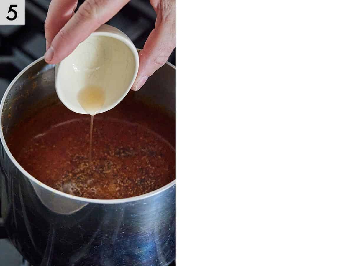 Instructional photo showing apple cider vinegar being adding to enchilada sauce in a pot.