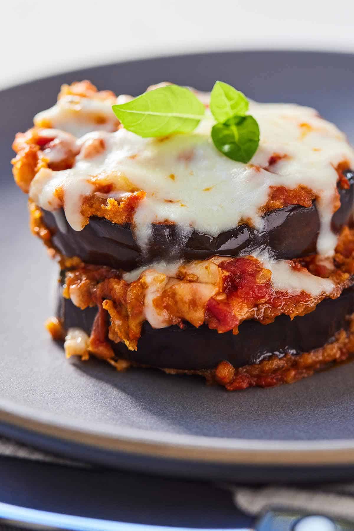 A plate with a serving of eggplant parmesan topped with basil.