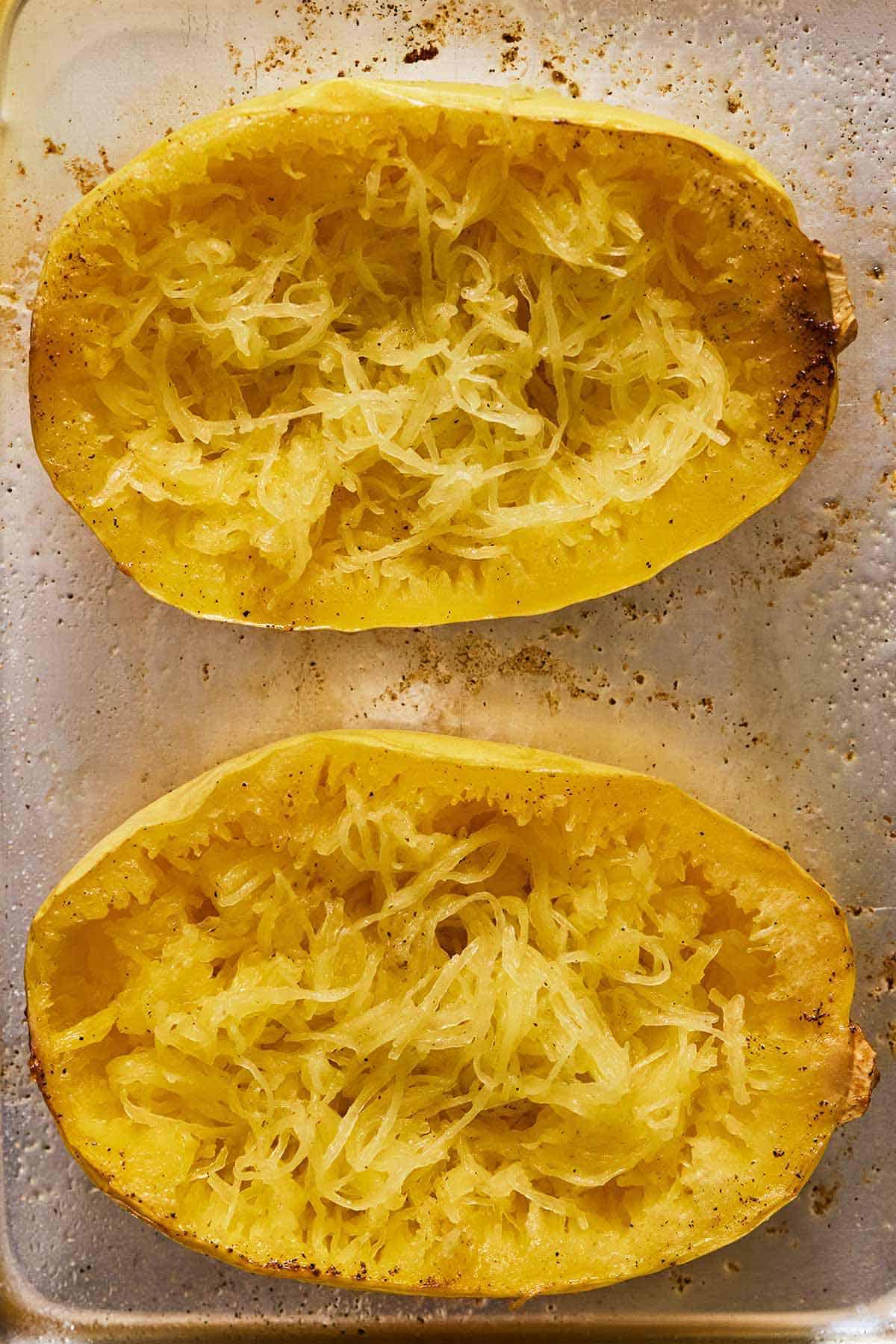 Two spaghetti squash on a sheet pan with the noodles pulled out.