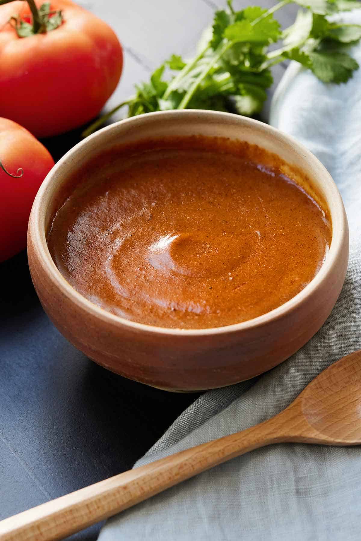 A bowl of homemade enchilada sauce beside linen and a wooden spoon.
