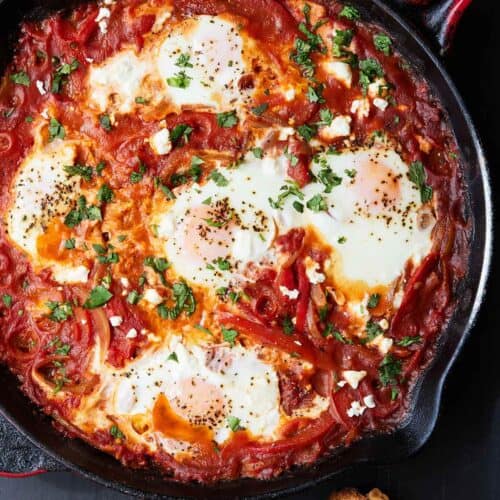 Overhead view of a cast iron containing shakshuka with cilantro and sliced bread beside it.