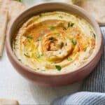 Pinterest graphic of a bowl of hummus with pita bread surrounding it.