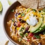 Pinterest graphic of a bowl of chicken tortilla soup with tortilla chips, avocado, sour cream, and shredded cheese on top.