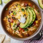 Pinterest graphic of an overhead view of a bowl of chicken tortilla soup with three slices of avocado, sour cream, and shredded cheese.