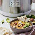 Pinterest graphic of a bowl of chicken tortilla soup in front of a pressure cooker with chips, avocado, and lime wedges around it.