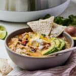 Pinterest graphic of a bowl of chicken tortilla soup topped with tortilla chips, sliced avocado, and shredded cheese in front of a pressure cooker.