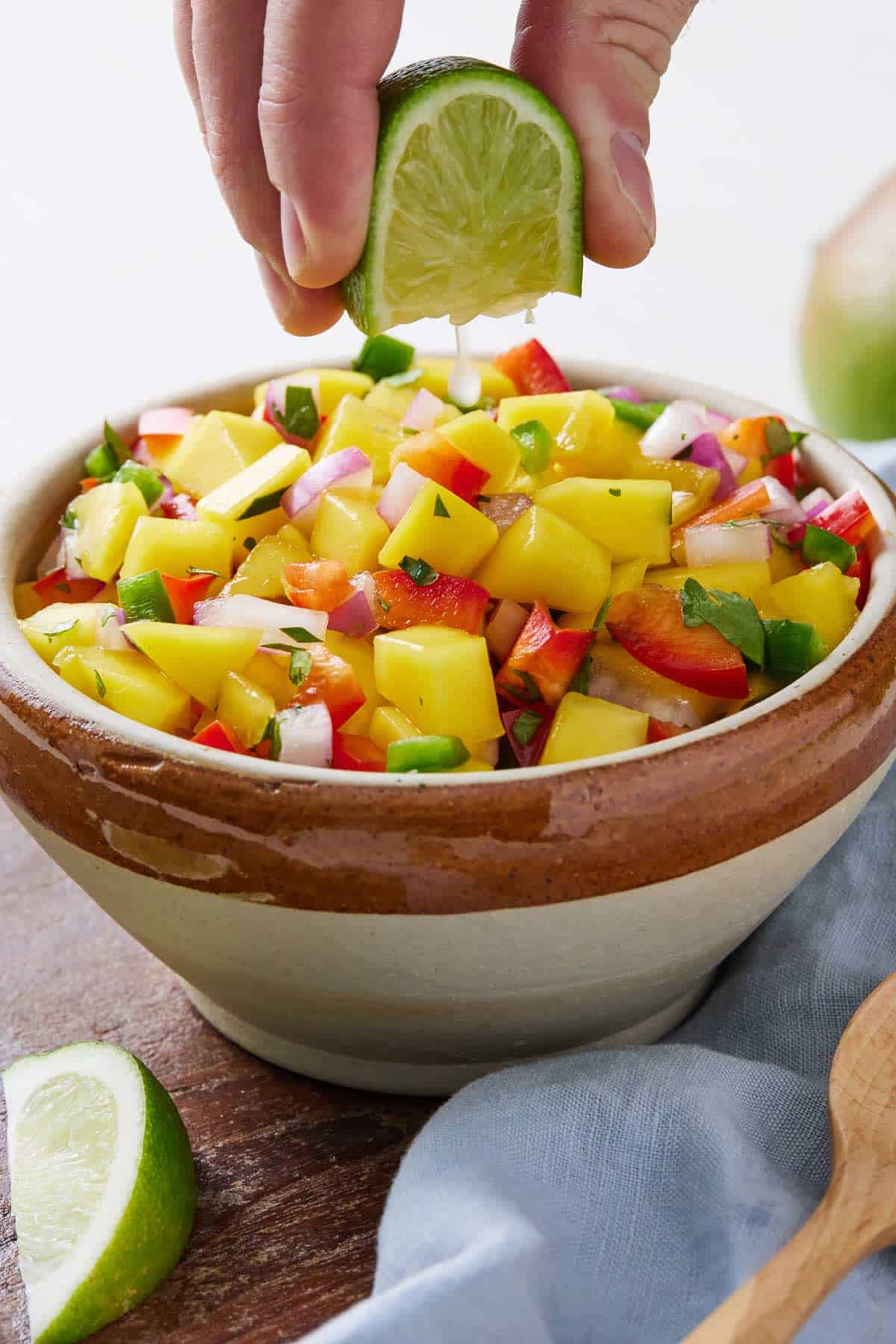 Lime being squeezed overtop of a bowl of mango salsa.