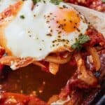 Pinterest graphic of the egg in shakshuka being lifted with a spoon from the pan.