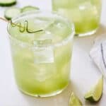 Pinterest graphic of two cucumber margarita with lime wedges around.
