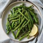 Overhead view of a plate of air fryer green beans with a lemon wedge.