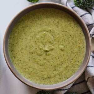 Overhead view of a bowl of cream of broccoli soup in a brown bowl with a striped linen napkin beside it.