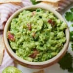 Close up of a bowl of guacamole with pieces of diced tomatoes mixed in.