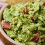 Pinterest image of a close up view of a bowl of guacamole with a chip tucked into the back of the bowl.