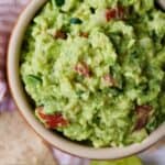 Pinterest image of a bowl of guacamole beside some tortilla chips and cilantro.