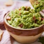 Pinterest image of a bowl of guacamole with a tortilla chip scooping some out.