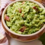 Pinterest image of a bowl of guacamole beside a pink linen napkin and tortilla chips.