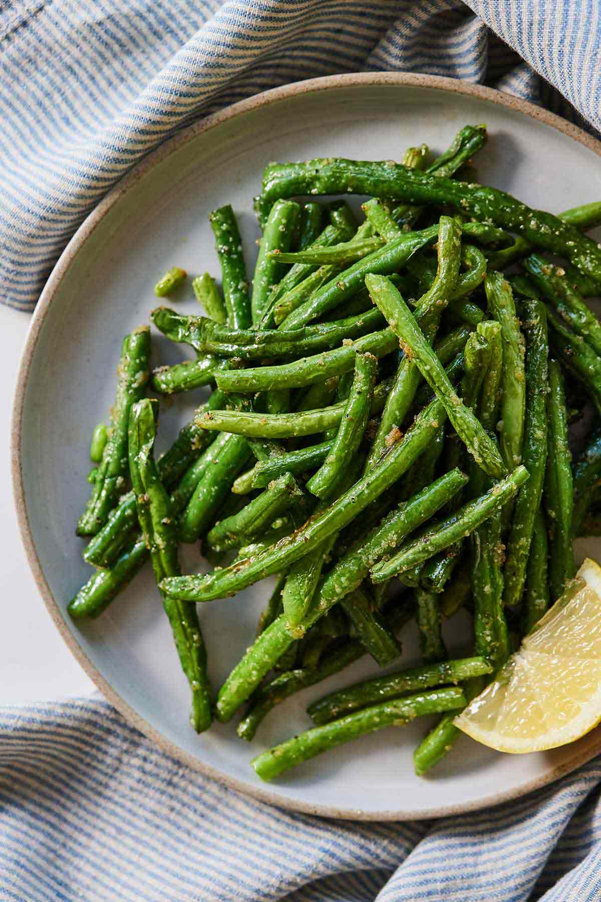 Overhead view of a plate of air fryer green beans with a lemon wedge surrounded by a blue striped linen napkin.