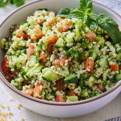 A bowl of tabbouleh topped with fresh mint as a garnish and beside a blue and white striped linen.