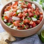Pinterest image of a bowl of pico de gallo beside a bunch of cilantro, tortilla chips, and a lime.