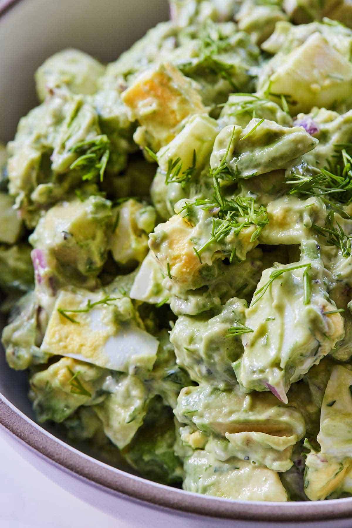 Close up of a bowl of avocado egg salad with fresh dill on top.