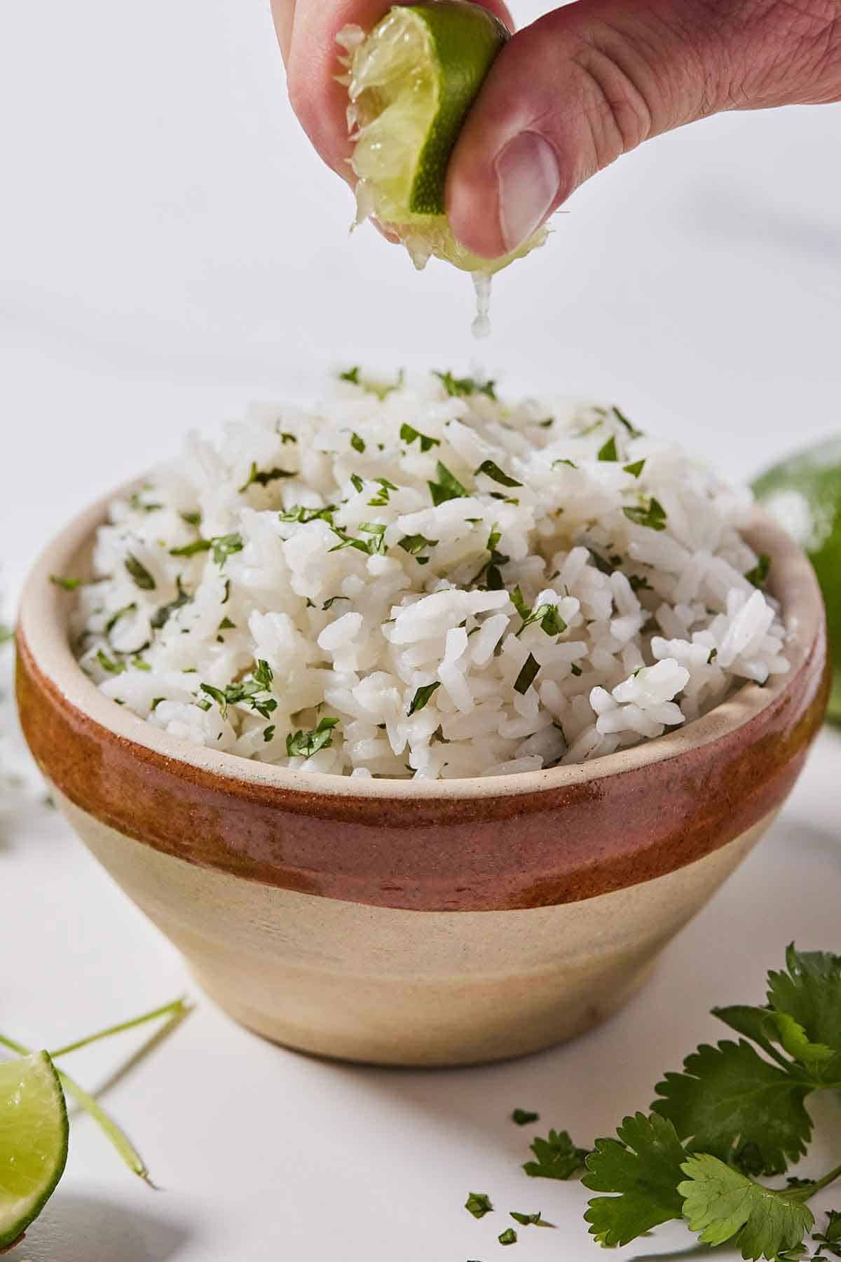 A bowl of cilantro lime rice with a lime wedge being squeezed over top of it.