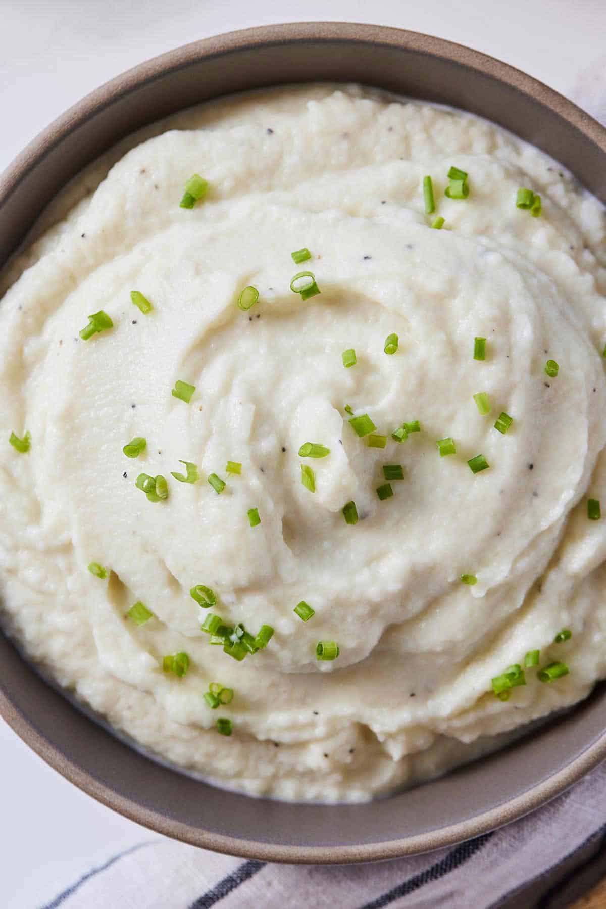 Overhead view of a bowl of mashed cauliflower with fresh chives on top.