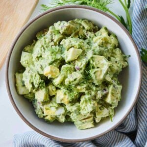 A bowl of avocado egg salad beside a striped linen napkin and some fresh dill.