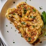 Pinterest graphic of a cauliflower steak on a white plate with parsley sprinkled on top.