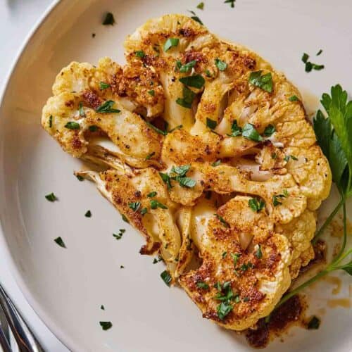 Overhead view of a plate of cauliflower steak with parsley garnished on top.