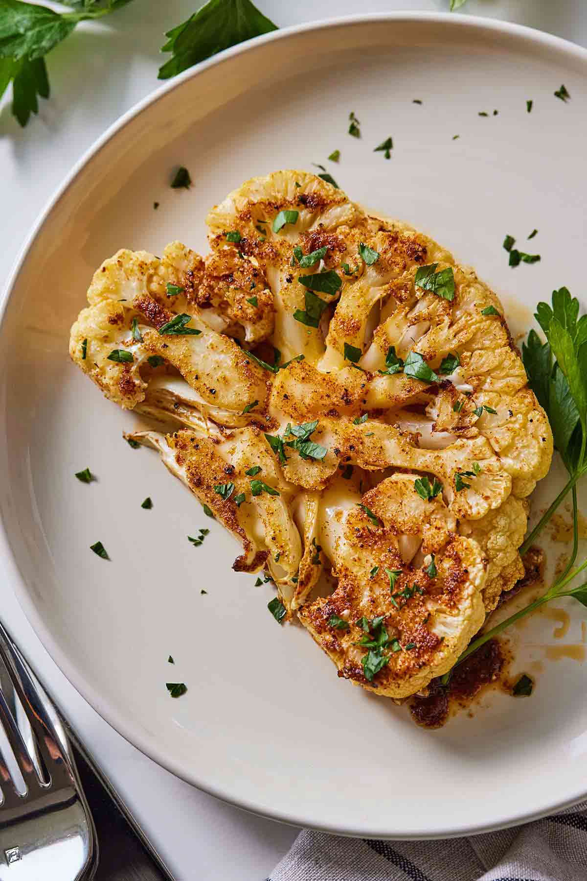 Overhead view of a plate of cauliflower steak with parsley garnished on top.